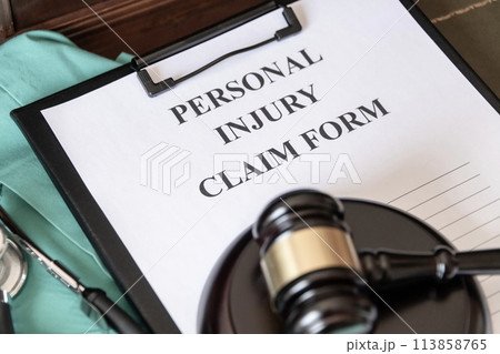 A personal injury claim form on a clipboard, accompanied by a stethoscope and medical scrubs, indicating health-related legal action. 113858765