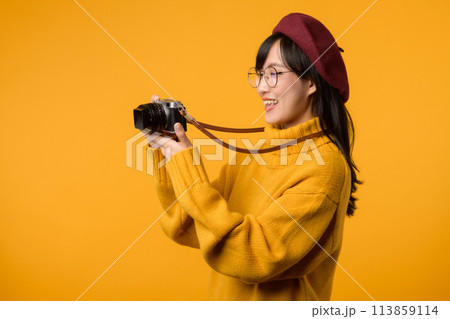 With her trusty camera in hand, a young Asian woman explores the world, embodying the spirit of a photographer in her stylish yellow sweater and red beret. 113859114