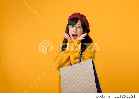A fashion savvy individual, sporting a red beret and yellow sweater, exults in a shopping spree against a vibrant yellow background. 113859251