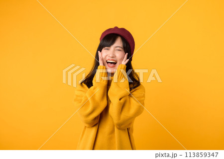 Young Asian woman laughing joyfully in a yellow sweater and red beret, radiating happiness against a sunny yellow background. Young Asian woman laughing joyfully in a yellow sweater and red beret, radiating happiness against a sunny yellow background. 113859347