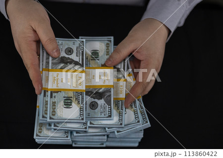 View from above. Hands holding stacks of hundred dollar bills close-up on a black background. Beautiful new money dollars in hands on a black background. Stacks of money in hands. 113860422