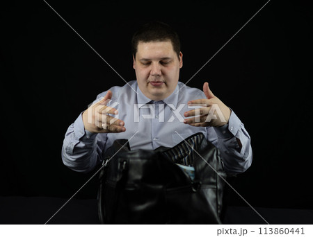 Male businessman folds stacks of hundred dollar bills into a large bag on a black background. A man collects money in a bag on the table. Concept money, million, wealth, dollars. 113860441