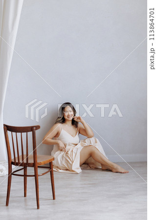 A woman is sitting on a wooden chair in a room with white walls A woman is sitting on a wooden chair in a room with white walls 113864701