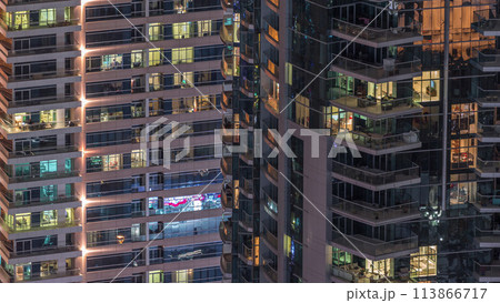 Rows of glowing windows with people in apartment building at night. 113866717