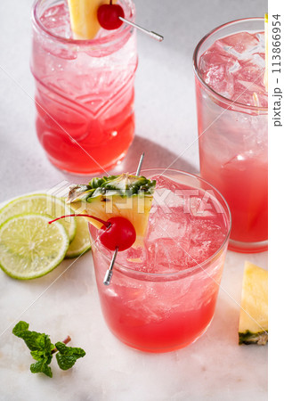 Singapore sling cocktails in a variety of glasses garnished with pineapple and cherry 113866954