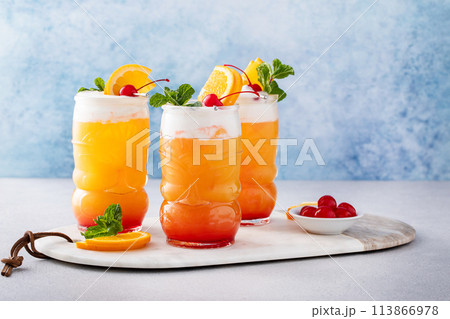 Tropical tiki cocktail with orange juice and rum in a fun tiki glass topped with cold foam 113866978