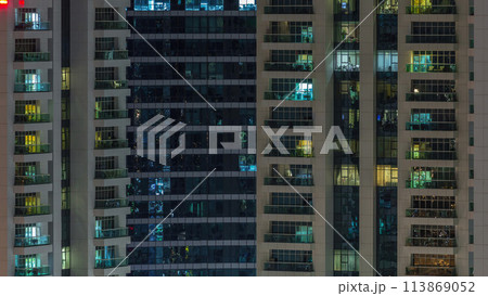 Rows of glowing windows with people in apartment building at night. 113869052
