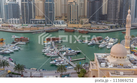 Yachts in Dubai Marina flanked by the Al Rahim Mosque and residential towers and skyscrapers aerial day to night timelapse. 113869252