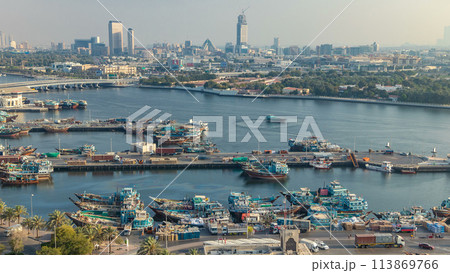 Dubai creek landscape timelapse with boats and ship in port and modern buildings in the background during sunset Dubai creek landscape timelapse with boats and ship in port and modern buildings in the background during sunset 113869766