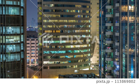 Windows of the multi-storey building of glass and steel lighting inside and moving people within timelapse 113869802
