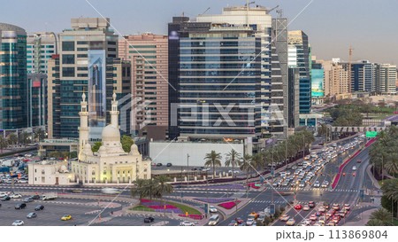 Mosque near Dubai Creek surrounded by modern buildings and busy traffic street day to night timelapse 113869804