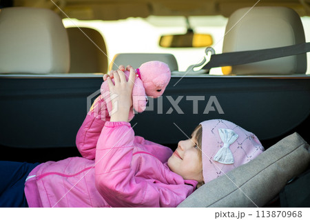 Pretty happy child girl playing with a pink toy teddy bear in a car trunk. 113870968