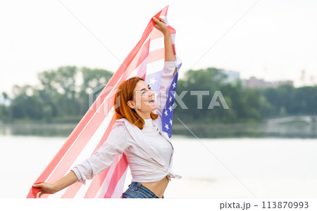 Portrait of happy smiling red haired girl with USA national flag in her hands. Positive young woman celebrating United States independence day. Portrait of happy smiling red haired girl with USA national flag in her hands. Positive young woman celebrating United States independence day. 113870993