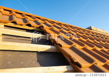 Overlapping rows of yellow ceramic roofing tiles mounted on wooden boards covering residential building roof under construction. 113871013