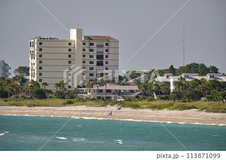 Resort beach with white sand, blue water, tall hotel buildings. Happy people sunbathing and swimming in ocean Resort beach with white sand, blue water, tall hotel buildings. Happy people sunbathing and swimming in ocean 113871099