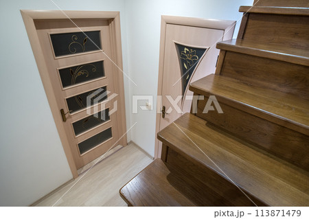 Interior of a house or appartment hallway with oak wooden stairs and room doors. 113871479