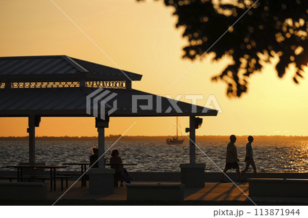 Dark silhouette of people resting under alcove roof on sea shore in public park at sunset Dark silhouette of people resting under alcove roof on sea shore in public park at sunset 113871944