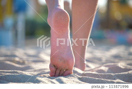 Close up of female feet walking barefoot on white grainy sand of golden beach on blue ocean water background 113871996