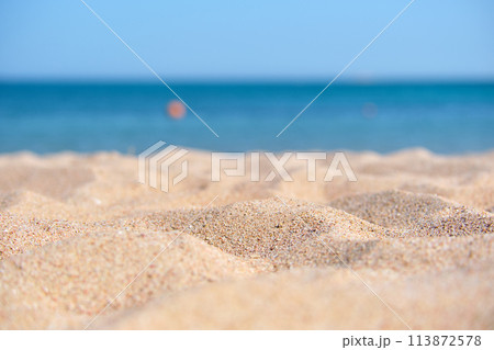 Close up of clean yellow sand surface covering seaside beach with blue sea water on background. Travel and vacations concept. Close up of clean yellow sand surface covering seaside beach with blue sea water on background. Travel and vacations concept. 113872578