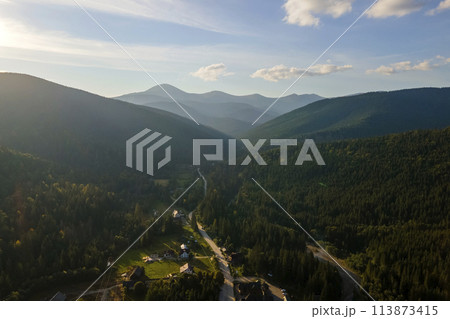 Aerial view of bright foggy morning over small rural homes between dark peaks with mountain forest trees at autumn sunrise. Beautiful scenery of wild woodland at dawn 113873415