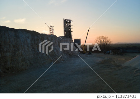 Cement factory at open pit mining of construction sand stone materials. Digging of gravel resources at quarry at sunset Cement factory at open pit mining of construction sand stone materials. Digging of gravel resources at quarry at sunset 113873433