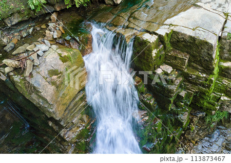 Waterfall on mountain river with white foamy water falling down from rocky formation in summer forest. 113873467
