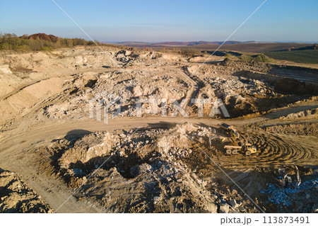Aerial view of open pit mining site of limestone materials for construction industry with excavators and dump trucks Aerial view of open pit mining site of limestone materials for construction industry with excavators and dump trucks 113873491