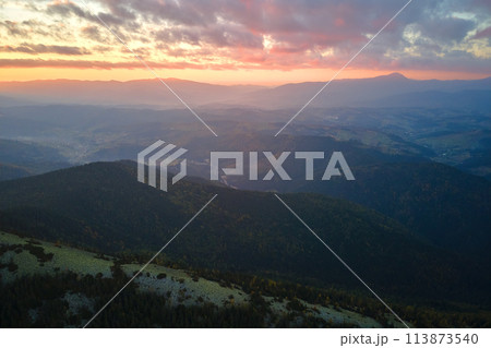 Aerial view of amazing scenery with foggy dark mountain peak covered with forest pine trees at autumn sunrise. Beautiful wild woodland with shining rays of light at dawn Aerial view of amazing scenery with foggy dark mountain peak covered with forest pine trees at autumn sunrise. Beautiful wild woodland with shining rays of light at dawn 113873540