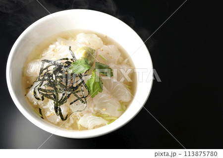 三つ葉、刻み海苔、わさびが乗った出汁入り熱々鯛茶漬けを黒背景で俯瞰撮影 113875780