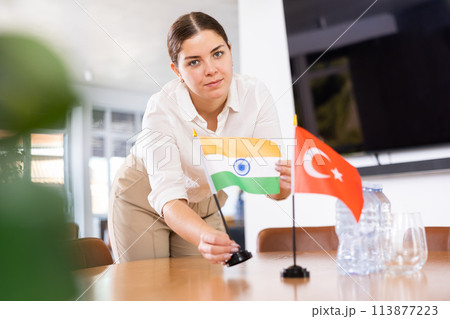 Young female assistant putting up turkish and indian flags on table for international negotiations Young female assistant putting up turkish and indian flags on table for international negotiations 113877223