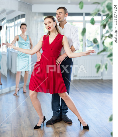Woman in red dancing passionate bachata with man at dance class 113877224