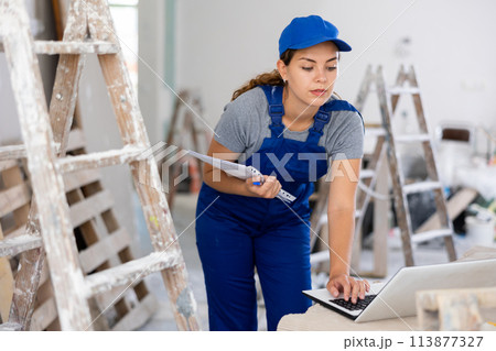 Woman builder checking documentation, using laptop 113877327