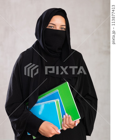 girl with face covered with burka holds lot of thick notebooks. foreign girl with face covered with burka holds lot of thick notebooks. foreign 113877413