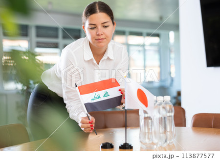 Businesswoman placing flags of Iraq and Japan on table before negotiations 113877577