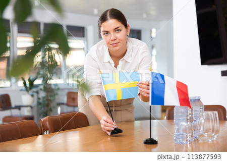 Young woman puts flags of Sweden and France on table Young woman puts flags of Sweden and France on table 113877593