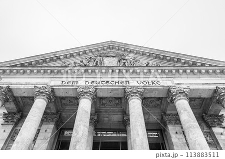 The monochrome facade of the Reichstag building, showcasing its iconic pillars and inscription: Dem Deutschen Volke. The seat of the German Bundestag, Berlin, Germany.. Black and white image. The monochrome facade of the Reichstag building, showcasing its iconic pillars and inscription: Dem Deutschen Volke. The seat of the German Bundestag, Berlin, Germany.. Black and white image. 113883511