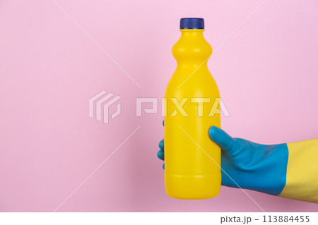 A hand with cleaning gloves holding a bottle of bleach on a pink background 113884455