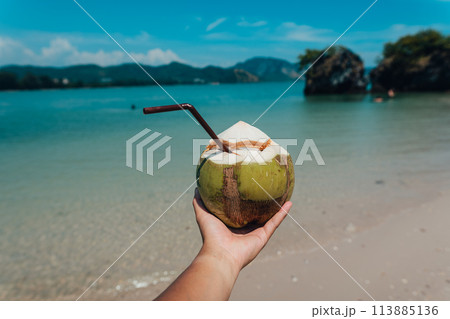coconut in hand at the beach on a summer day coconut in hand at the beach on a summer day 113885136