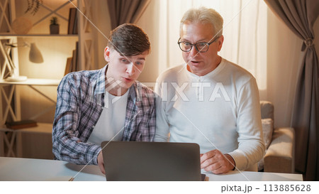 Family help. Internet leisure. Happy rest. Supportive son teaching overjoyed excited father how to use laptop at home. 113885628