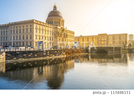 Golden morning sunlight bathes the Berlin Palace and Humboldt Forum, reflecting on the calm waters. Berlin, Germany 113886151