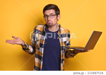 Studio shot of frustrated man holding laptop on yellow background Studio shot of frustrated man holding laptop on yellow background 113887516