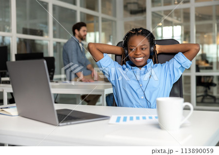 African American relaxed woman call center operator agent consulting customer wearing headset 113890059