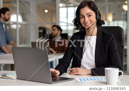 Young friendly operator woman agent with headsets working in call center in contemporary office 113890165