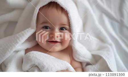 Baby wearing towel in white sunny bedroom. Newborn child relaxing in bed after bath or shower. Nursery for children. Textile and bedding for kids 113891300