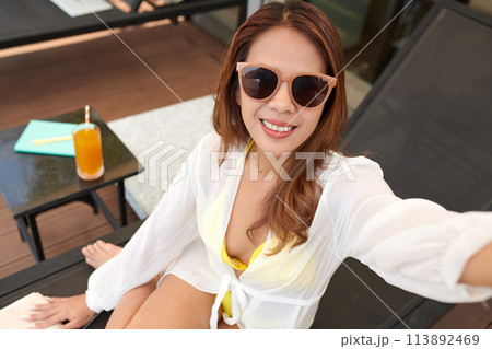 Cheerful woman in sunglasses taking selfie by swimming pool Cheerful woman in sunglasses taking selfie by swimming pool 113892469