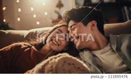 A young couple shares a cozy moment on the couch, radiating warmth and joy. 113895476