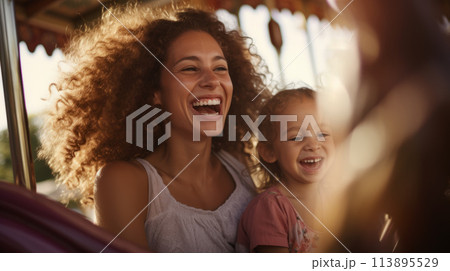 Mother and child share smiles on a sunny carousel ride, radiating pure joy on a warm summer day. 113895529