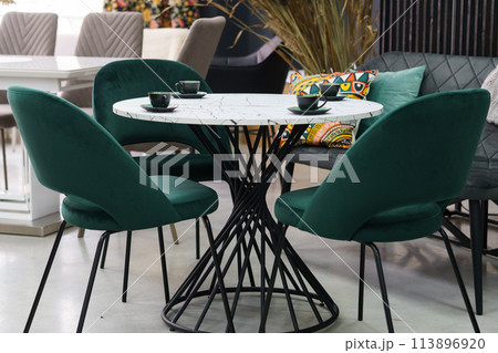 White wooden table complete with green wooden chairs with soft fabric upholstery. Green cups on the table 113896920