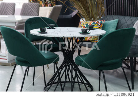 White wooden table complete with green wooden chairs with soft fabric upholstery. Green cups on the table 113896921