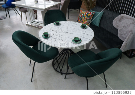 White wooden table complete with green wooden chairs with soft fabric upholstery. Green cups on the table 113896923